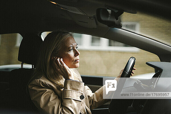 Geschäftsfrau stellt In-Ear-Kopfhörer beim Autofahren ein