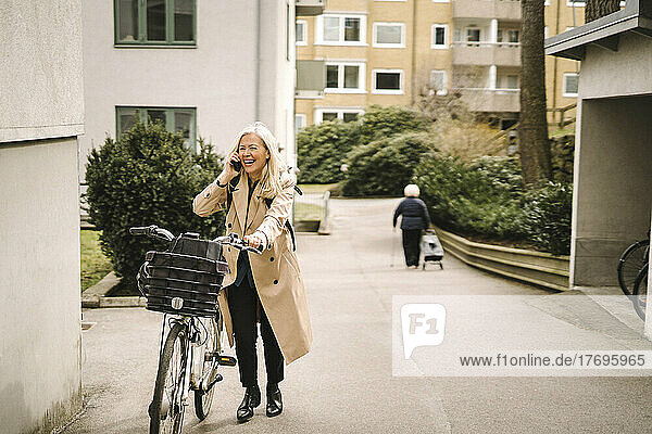 Glückliche Geschäftsfrau  die mit ihrem Smartphone telefoniert  während sie auf dem Fußweg Fahrrad fährt