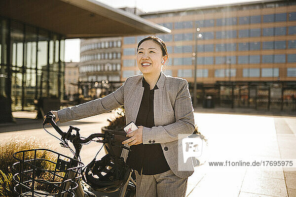 Glückliche weibliche Fachkraft  die an einem sonnigen Tag auf einem Fußweg Fahrrad fährt