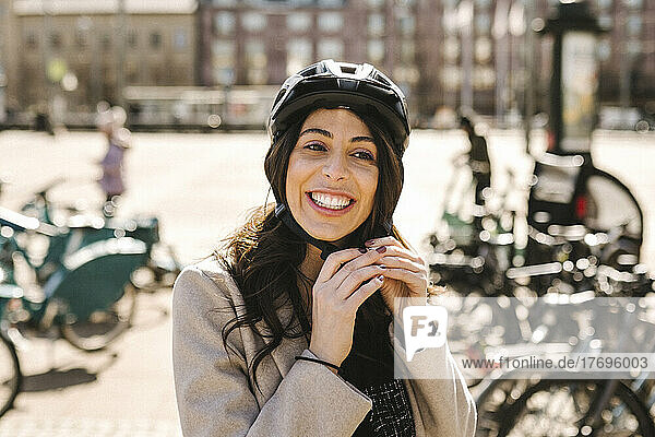 Glückliche Geschäftsfrau mit Helm an einer Fahrradabstellanlage in der Stadt