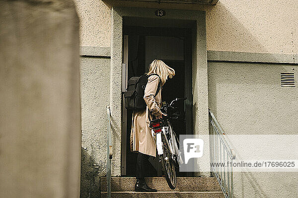 Geschäftsfrau in voller Länge beim Betreten eines Gebäudes mit Elektrofahrrad