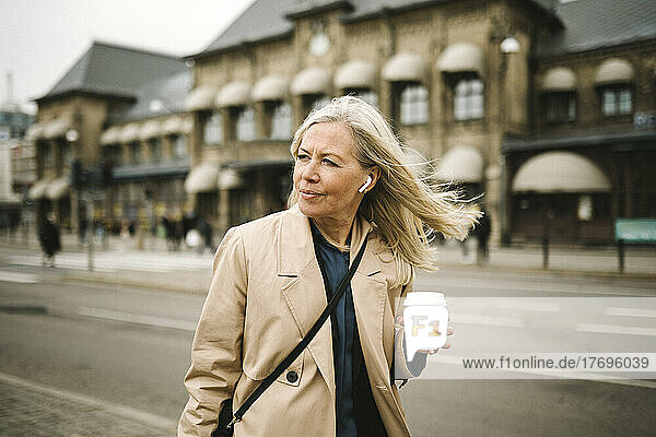 Businesswoman looking away while holding disposable coffee cup in city