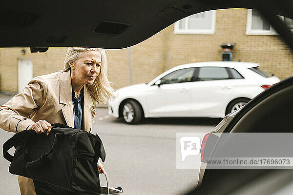 Blonde Geschäftsfrau lädt Gepäck in den Kofferraum eines Autos