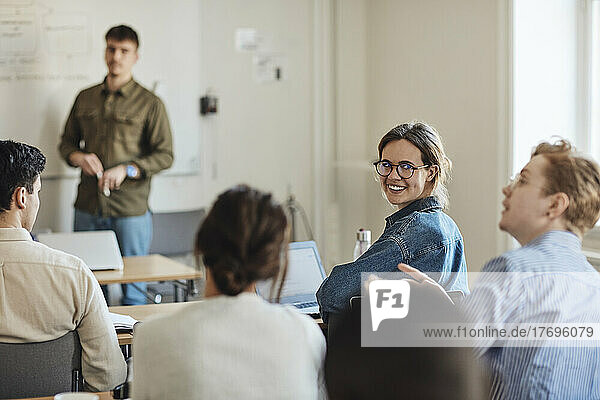 Smiling female student looking at friend during lecture in classroom