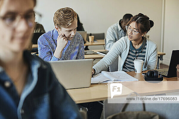 Eine Schülerin hilft einem männlichen Freund  während sie am Schreibtisch im Klassenzimmer sitzt