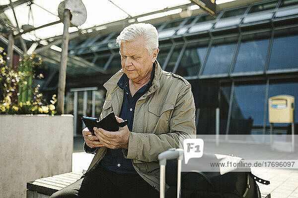 Geschäftsmann  der sein Smartphone benutzt  während er auf einer Bank am Bahnhof sitzt