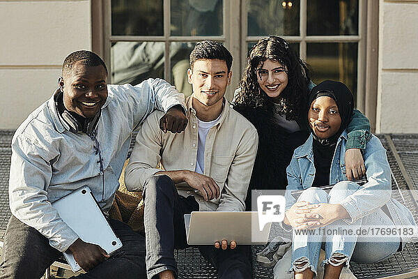 Portrait of multiracial students with laptop sitting at university campus