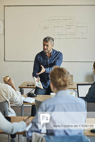 Male teacher gesturing while teaching students classroom