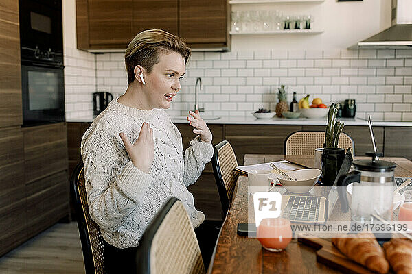 Lesbische Berufstätige gestikulieren während eines Videoanrufs über einen Laptop am Esstisch zu Hause