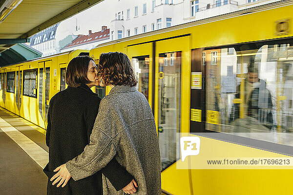 Lesbisches Paar  das sich küsst  während es an einem gelben Zug am Bahnhof steht