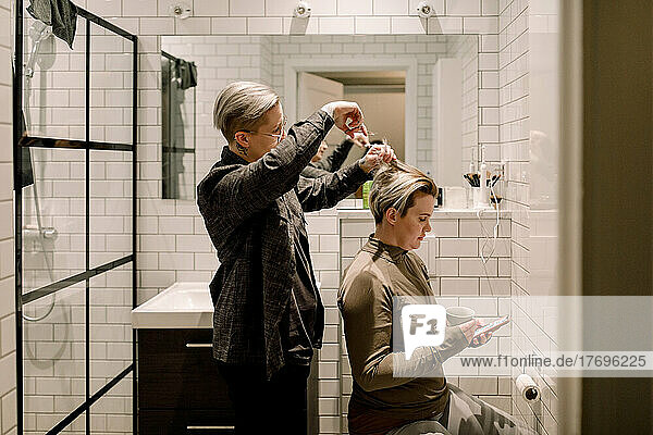 Side view of lesbian woman cutting hair of girlfriend in bathroom at home