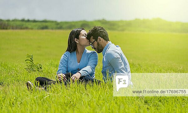 Romantisches Paar sitzt im Gras und küsst sich auf die Stirn  Ein hübsches Mädchen küsst die Stirn ihres Freundes auf dem Feld  Ein verliebtes Paar sitzt auf dem Feld und küsst sich auf die Stirn