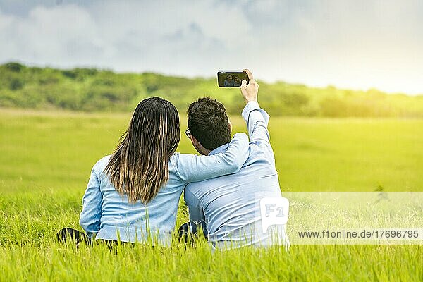 Junges verliebtes Paar macht ein Selfie im Feld  Verliebte machen Selfies im Feld mit ihrem Smartphone  Lächelndes verliebtes Paar sitzt im Gras und macht Selfies