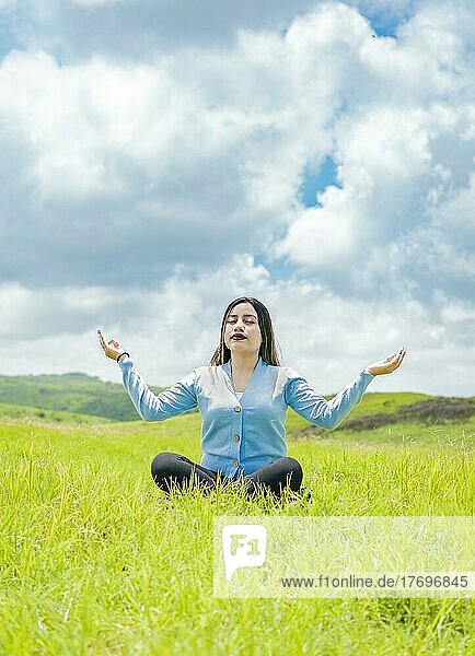 Junge Frau macht Yoga auf dem Gras im Feld mit blauem Himmel im Hintergrund  Mädchen sitzt und macht Meditation Yoga auf dem Feld  Frau macht Yoga im Freien