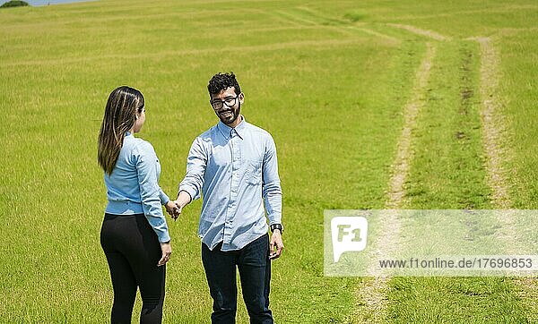 Zwei lächelnde Verliebte auf dem Feld  die sich an den Händen halten  Schönes Paar  das sich auf dem Feld anschaut  zwei Personen  die sich auf dem Feld an den Händen halten