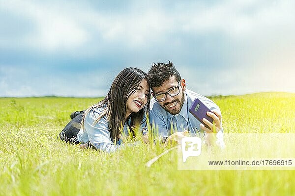 Ein Paar  das im Gras liegt und ein Selfie macht  ein junges verliebtes Paar  zwei verliebte Menschen  die im Gras liegen und Selfies machen
