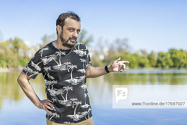 Bearded mature man in a lake looking at the camera with one arm akimbo and the other pointing to the side. Copy space