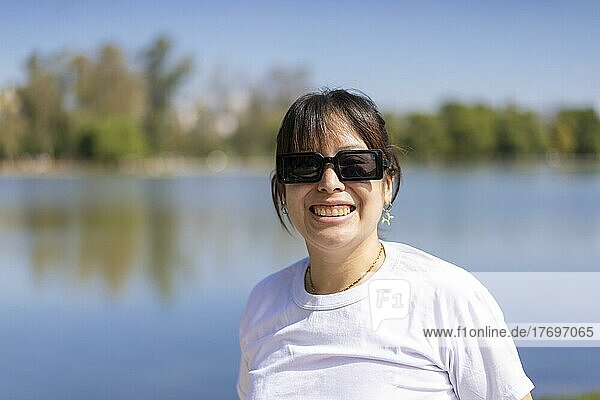 Porträt einer jungen lateinischen Frau  die lächelnd in die Kamera schaut  an einem See mit Kopierraum