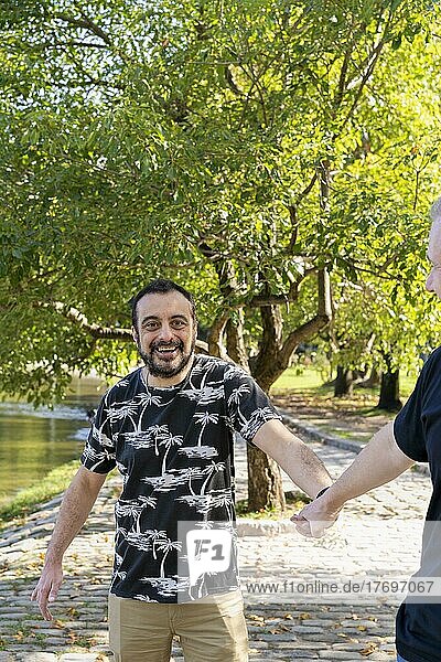 Ein schwuler Mann ist überrascht und glücklich  weil sein Freund in der Öffentlichkeit seine Hand hält  während sie an einem See spazieren gehen. Coming-out-Konzept
