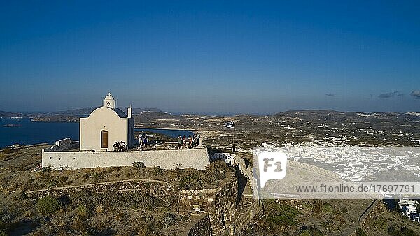 Drone shot  evening light  summit chapel Messa Panagia  people in front of the chapel  blue almost cloudless sky  main town  Plaka  Milos Island  Cyclades  Greece  Europe