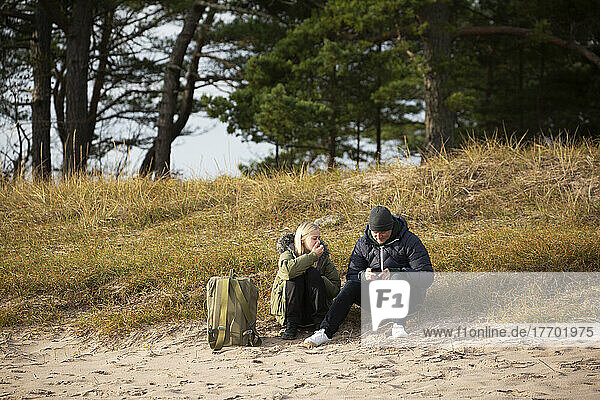 Father and daughter sitting in grass by beach