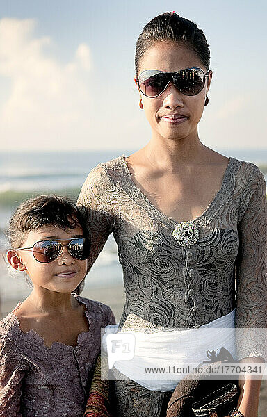 Eine Mutter und eine Tochter mit Sonnenbrille an einem Strand am Rande des Wassers; Bali