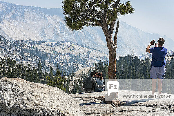 At Olmstead Point  smoke from a wildfire clouds the view of Yosemite National Park  California  as a couple embraces and a man photographs; California  United States of America