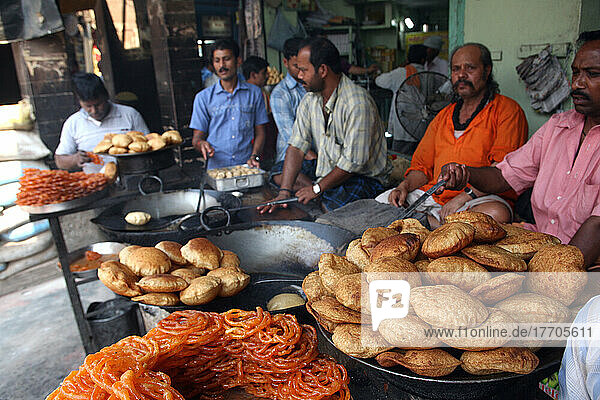 Herstellung von indischen frittierten Snacks  darunter Puri  indisches frittiertes Brot  vor diesem Lebensmittelcafé in Varanasi. Die Kultur von Varanasi ist eng mit dem Fluss Ganges und seiner religiösen Bedeutung verbunden und gilt als religiöse Hauptstadt Indiens .