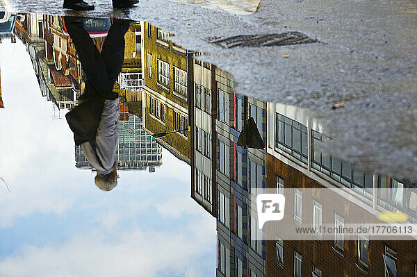 Gebäude und ein Fußgänger  der sich in einer Wasserpfütze auf der Straße spiegelt  Soho; London  England