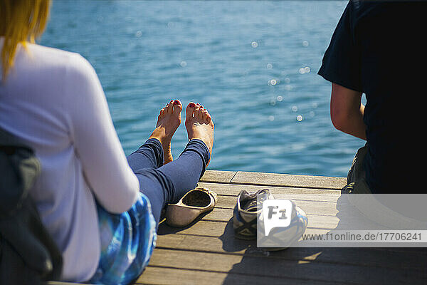 Zwei Menschen sitzen auf einem hölzernen Dock am Rande des Wassers; Barcelona  Spanien