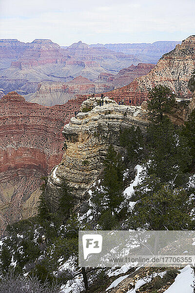 Wide angle vertical frame of the Grand Canyon in winter with tourists chatting and taking photographs on an outcrop; Arizona  United States of America