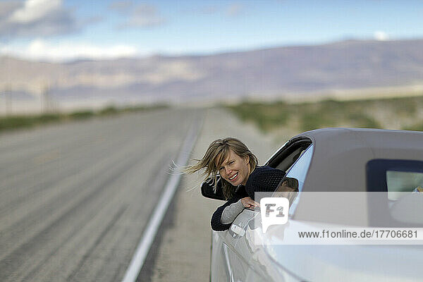 Eine junge Frau lehnt sich aus ihrem Autofenster auf einer verlassenen Straße in der Wüste auf dem Highway 190; Kalifornien  Vereinigte Staaten von Amerika