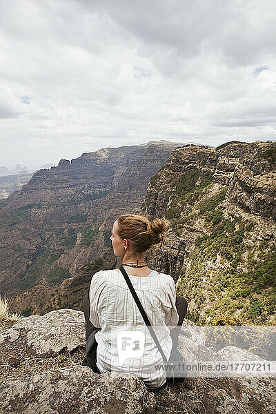 Eine junge Frau sitzt auf einem Bergrücken mit Blick auf die spektakulären Simien-Berge; Äthiopien