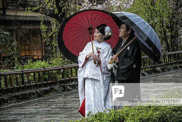 Couple in the historic area of Kyoto wearing traditional dress for an evening walk in the rain; Kyoto  Japan