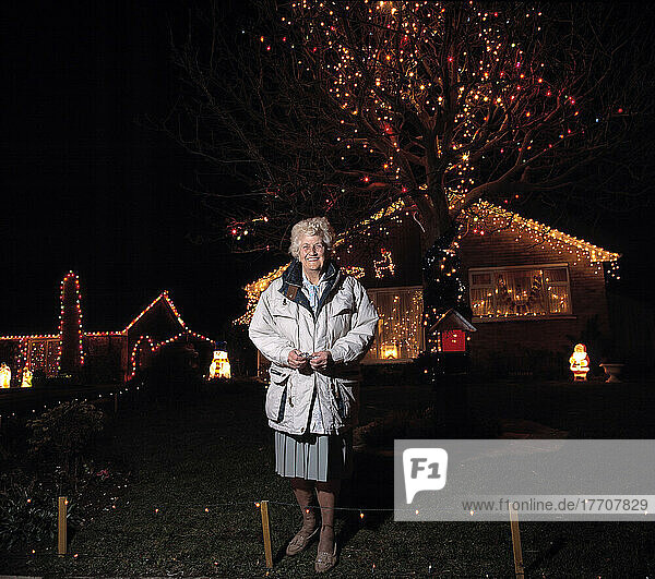 Frau  die vor einem weihnachtlich geschmückten Haus steht (Weihnachtsbeleuchtung und -dekoration)  Uk.