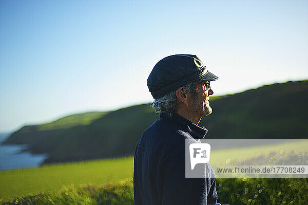 Ein Mann mit Sonnenlicht auf seinem Gesicht schaut mit einer üppigen Landschaft im Hintergrund  Lleyn Peninsula; Wales