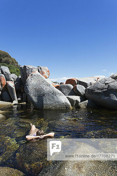Eine junge Frau schwimmt allein unter den großen Felsen vor dem Bay Of Fires Beach; Tasmanien  Australien