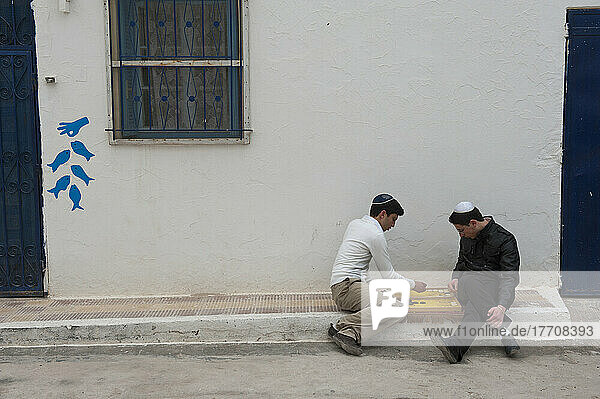 Zwei Jungen im Teenageralter spielen ein Brettspiel auf dem Bürgersteig vor ihrem Haus in der jüdischen Stadt Erriadh; Erriadh  Djerba  Tunesien