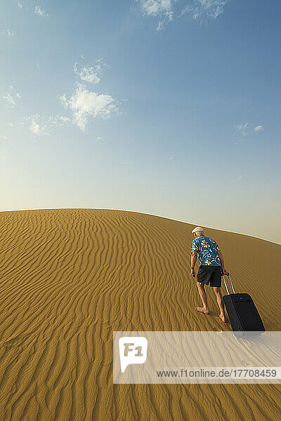 Barefoot Man With Suitcase Walking Up Sand Dune; Dubai  United Arab Emirates