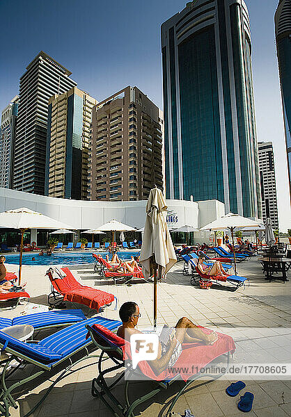 Tourists Lounging On Deckchairs By Hotel Pool With Skyscrapers In Background  Dubai's International Financial Centre  Sheikh Zayed Road Dubai  Uae. Middle East