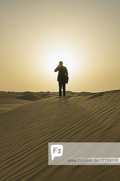 Man In Smart Suit Making Phone Call On Top Of Sand Dune At Dusk  Dubai  Vereinigte Arabische Emirate