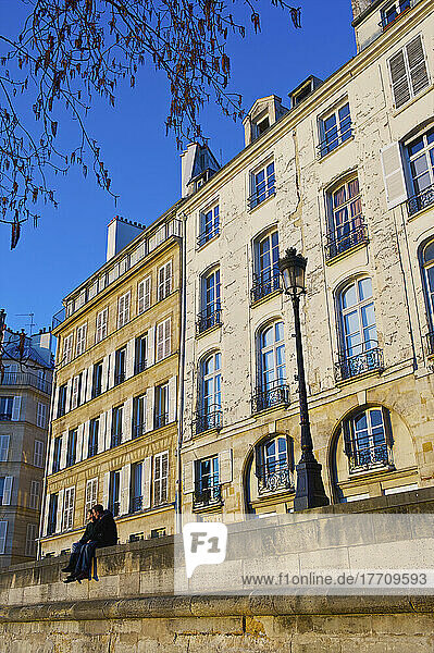 Ein Paar sitzt zusammen auf einer Mauer neben einem Laternenpfahl vor einem Wohnhaus; Paris  Frankreich