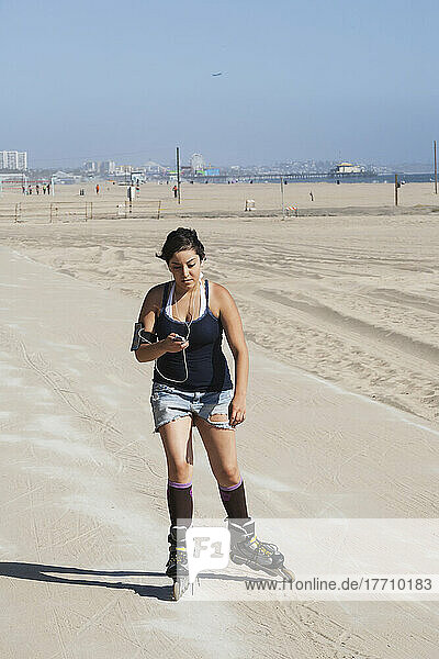 Eine junge Frau mit Inline-Skates auf der Promenade entlang der Küste mit Ohrstöpseln und einem Mobiltelefon; Kalifornien  Vereinigte Staaten von Amerika