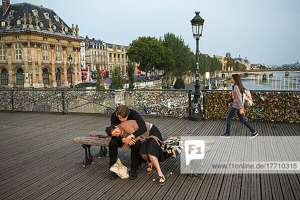 At dawn on Pont des Arts  or the Love Lock Bridge  a couple embraces while sitting on a bench in Paris  France