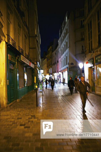 Fußgänger auf einem Gehweg außerhalb von Einzelhandelsgebäuden bei Nacht; Paris  Frankreich