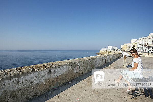 A Woman Sits On A Bench On A Promenade Overlooking The Water  Gallipoli; Salento  Italy