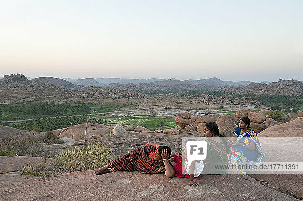 Drei Frauen und ein Mädchen sitzen auf einem Felsen und blicken auf die Landschaft; Hampi  Karnataka  Indien