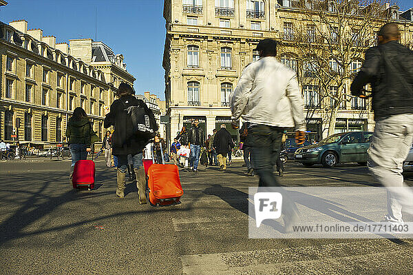 Fußgänger  die eine Straße an einer Kreuzung überqueren  einige von ihnen rollen Gepäck hinter sich her; Paris  Frankreich
