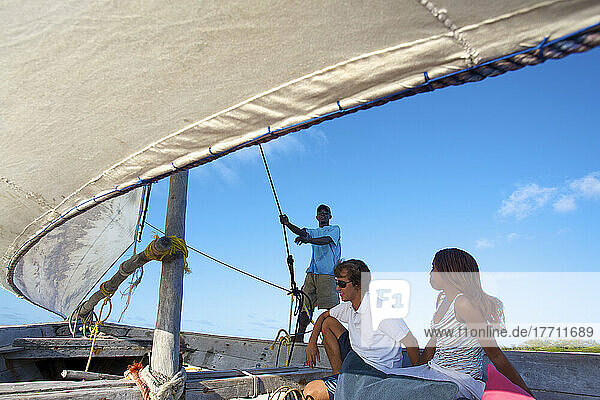Ein Mann und eine Frau sitzen an Bord eines Segelboots  während ein Mann das Segel festhält; Insel Vamizi  Mosambik