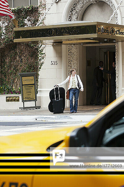 Eine Frau wartet mit ihrem Gepäck auf eine Mitfahrgelegenheit auf der Straße vor einem Hotel; Kalifornien  Vereinigte Staaten von Amerika